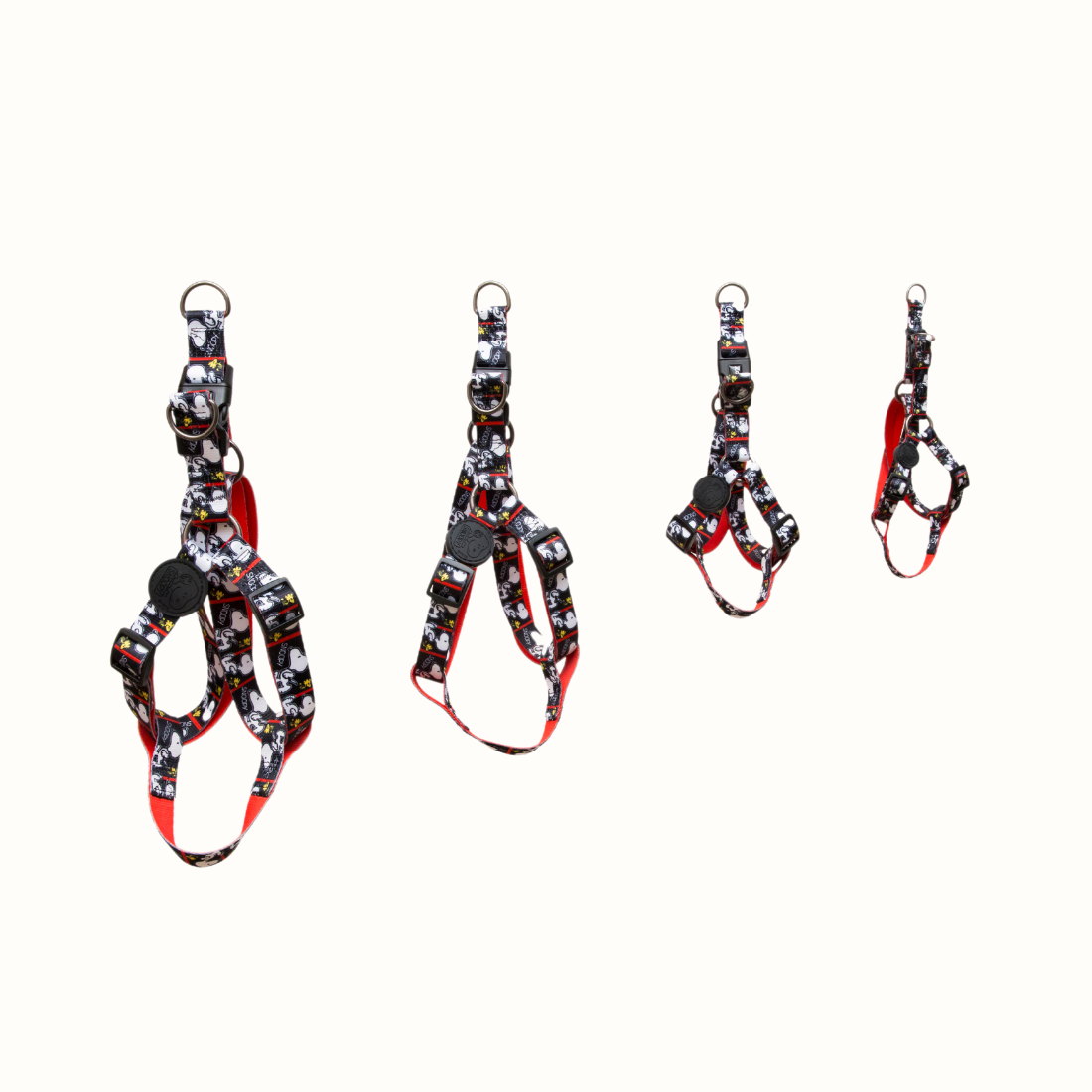 Arnês Zooz, de cores preto e branco com detalhes vermelhos e figuras do snoopy. Vista de frente, de varios tamanhos, sobre fundo branco.