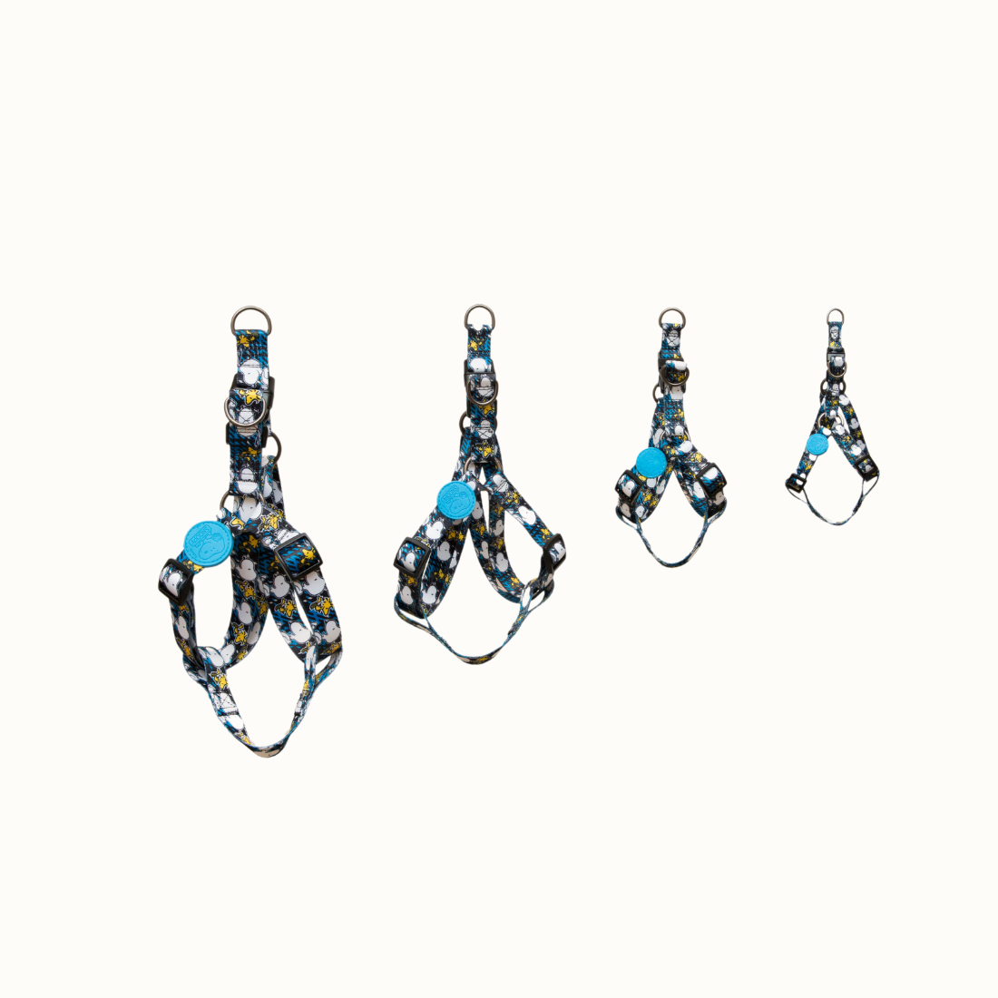 Arnês Zooz, em padrão azul e preto, com figuras do snoopy e do Woodstock, em vários tamanhos. Vista de frente, sobre fundo branco.