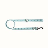 Trela Zooz, em padrão azul claro e verde claro e figuras do snoopy. Vista de frente, sobre fundo branco.