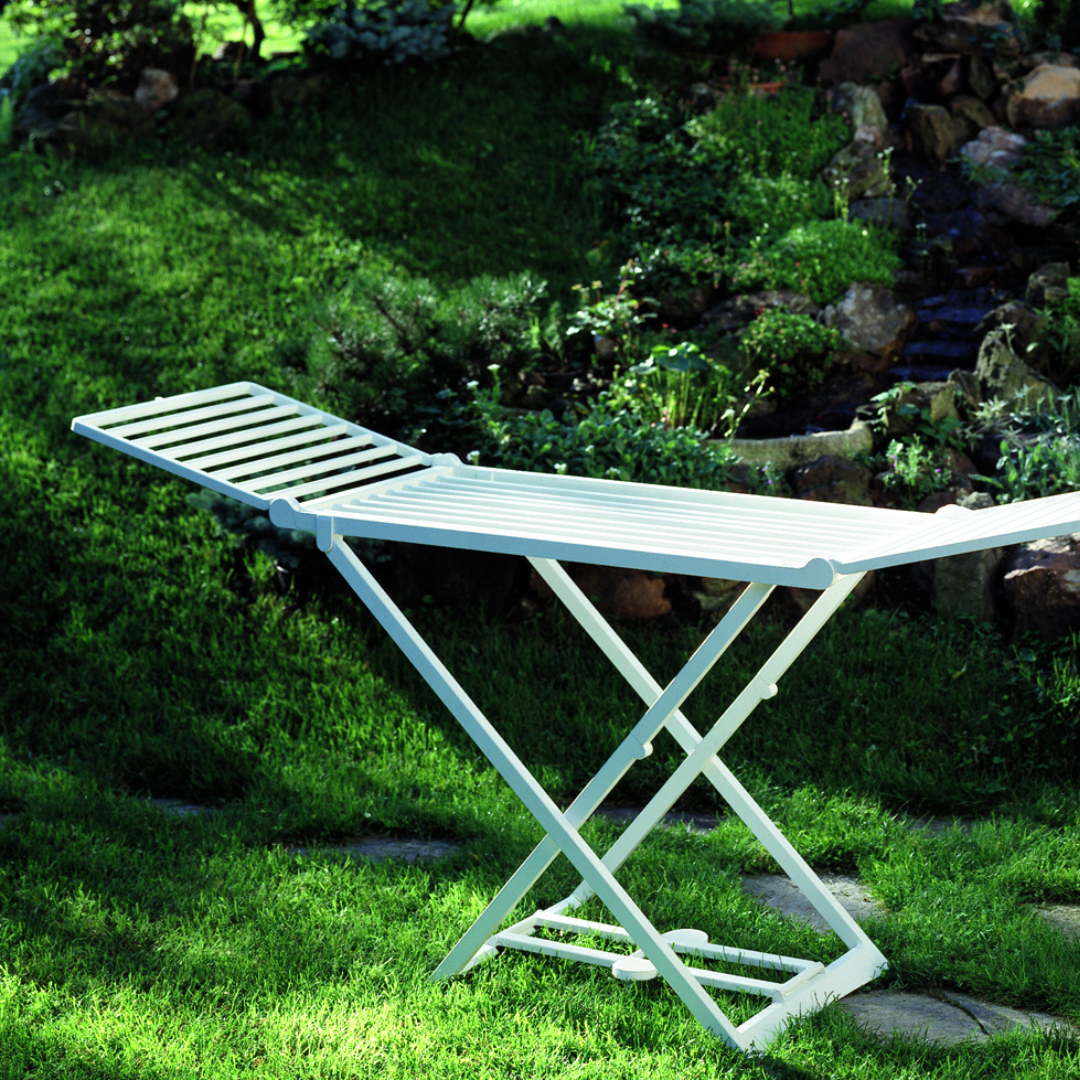 Estendal de roupa IPAE PROGARDEN em plástico branco, com estrutura dobrável em formato de X e hastes horizontais para suporte das peças. Exibido em ambiente externo.