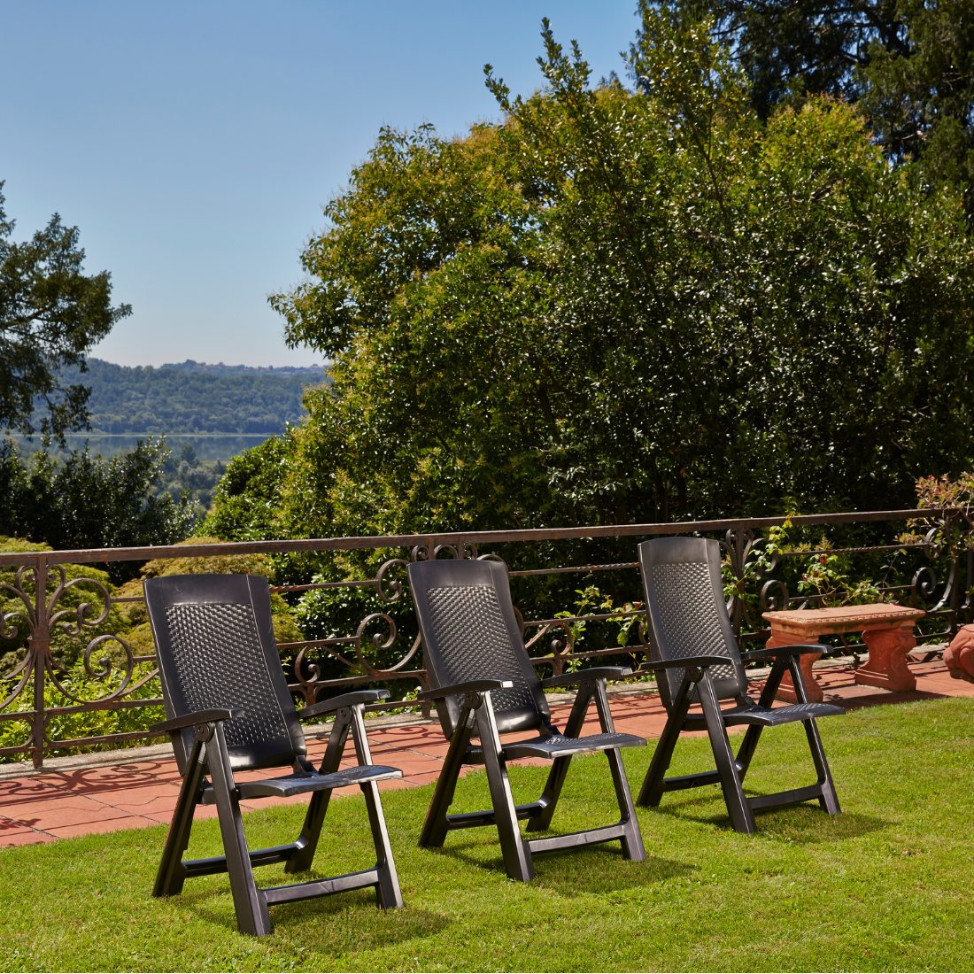 Cadeira dobrável IPAE PROGARDEN em plástico cinzento, com assento e encosto com padrão entrançado, exibida em ambiente exterior e com vista frontal ligeiramente inclinada para a direita.