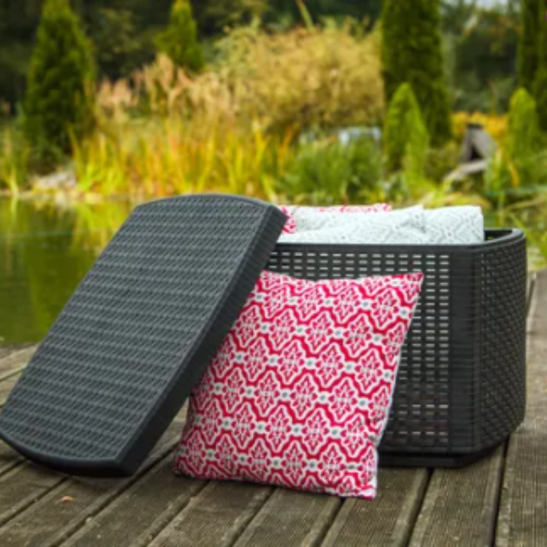 Mesa com arrumação IPAE PROGARDEN em plástico, de cor cinzenta, com acabamento trançado. Exibido em ambiente exterior e com tampa aberta.