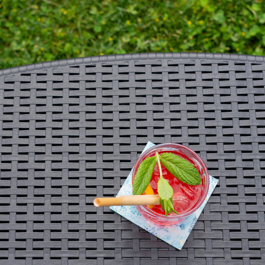 Mesa com arrumação IPAE PROGARDEN em plástico, de cor cinzenta, com acabamento trançado. Vista em pormenor e exibida em ambiente exterior.