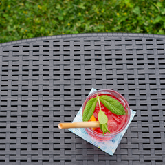 Mesa com arrumação IPAE PROGARDEN em plástico, de cor cinzenta, com acabamento trançado. Vista em pormenor e exibida em ambiente exterior.