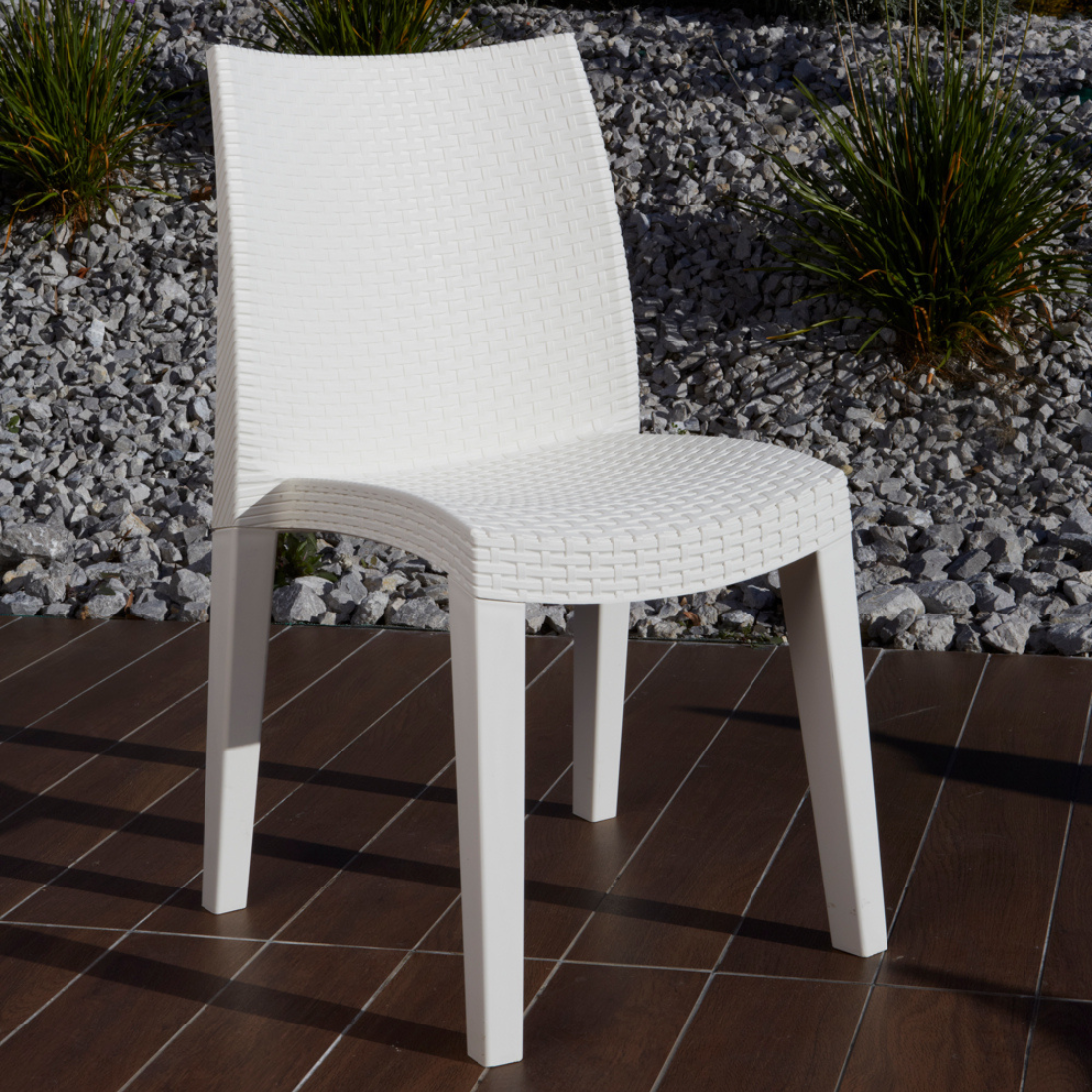 Cadeira IPAE PROGARDEN em plástico, de cor branca, com encosto e assento com acabamento trançado. Exibido em ambiente exterior.
