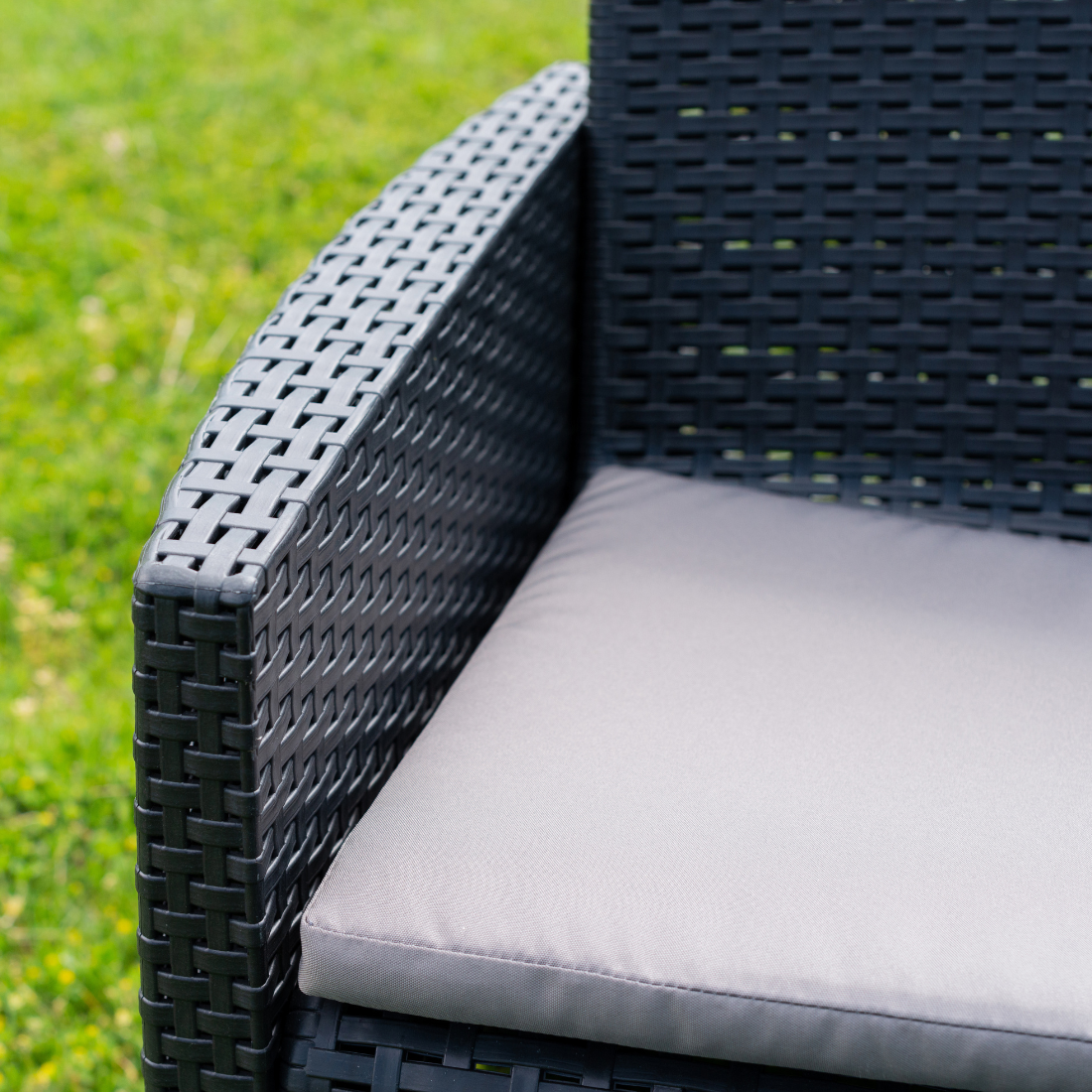 Cadeirão IPAE PROGARDEN com acabamento entrançado, de cor cinzenta, almofada no assento e com braços de apoio. Visto ao pormenor, sobre fundo branco.