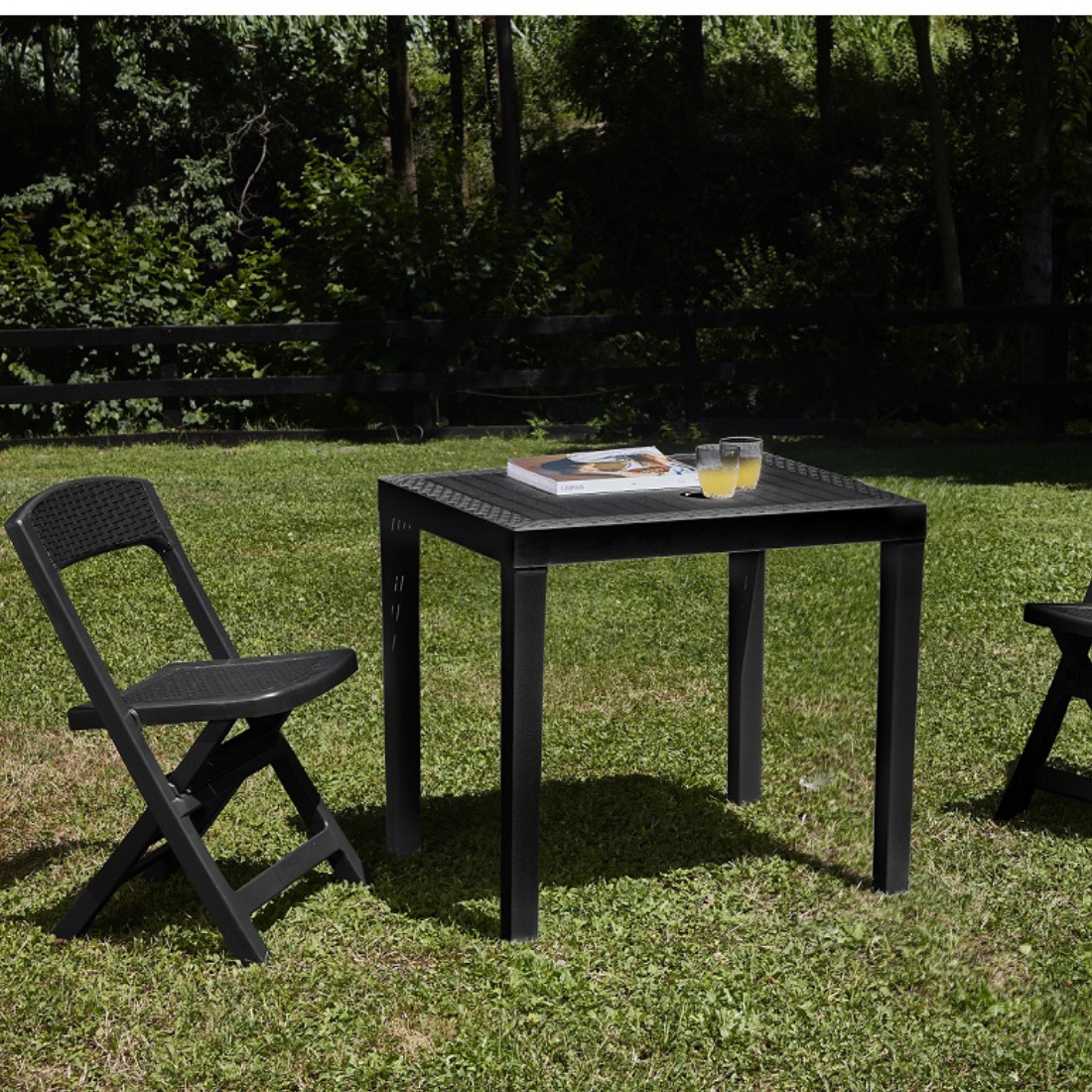 Conjunto de mesa desmontável e duas cadeiras dobráveis IPAE PROGARDEN em plástico, de cor cinzenta, com acabamento trançado. Exibido em ambiente exterior.