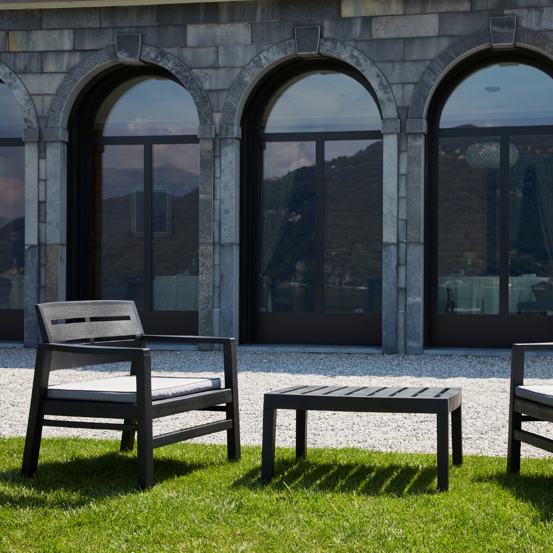 Conjunto composto por duas cadeiras com braços e encosto de apoio, acompanhadas de almofadas no assento, e uma mesa baixa IPAE PROGARDEN. Exibido em ambiente exterior.