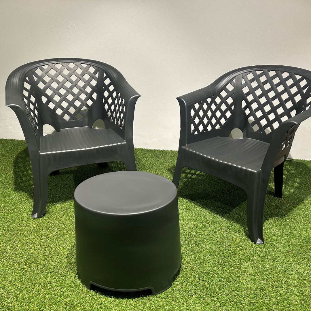 Conjunto de duas cadeiras com braços e encosto vazado em padrão quadriculado e uma mesa IPAE PROGARDEN, em plástico, na cor preta, exibida em ambiente exterior.