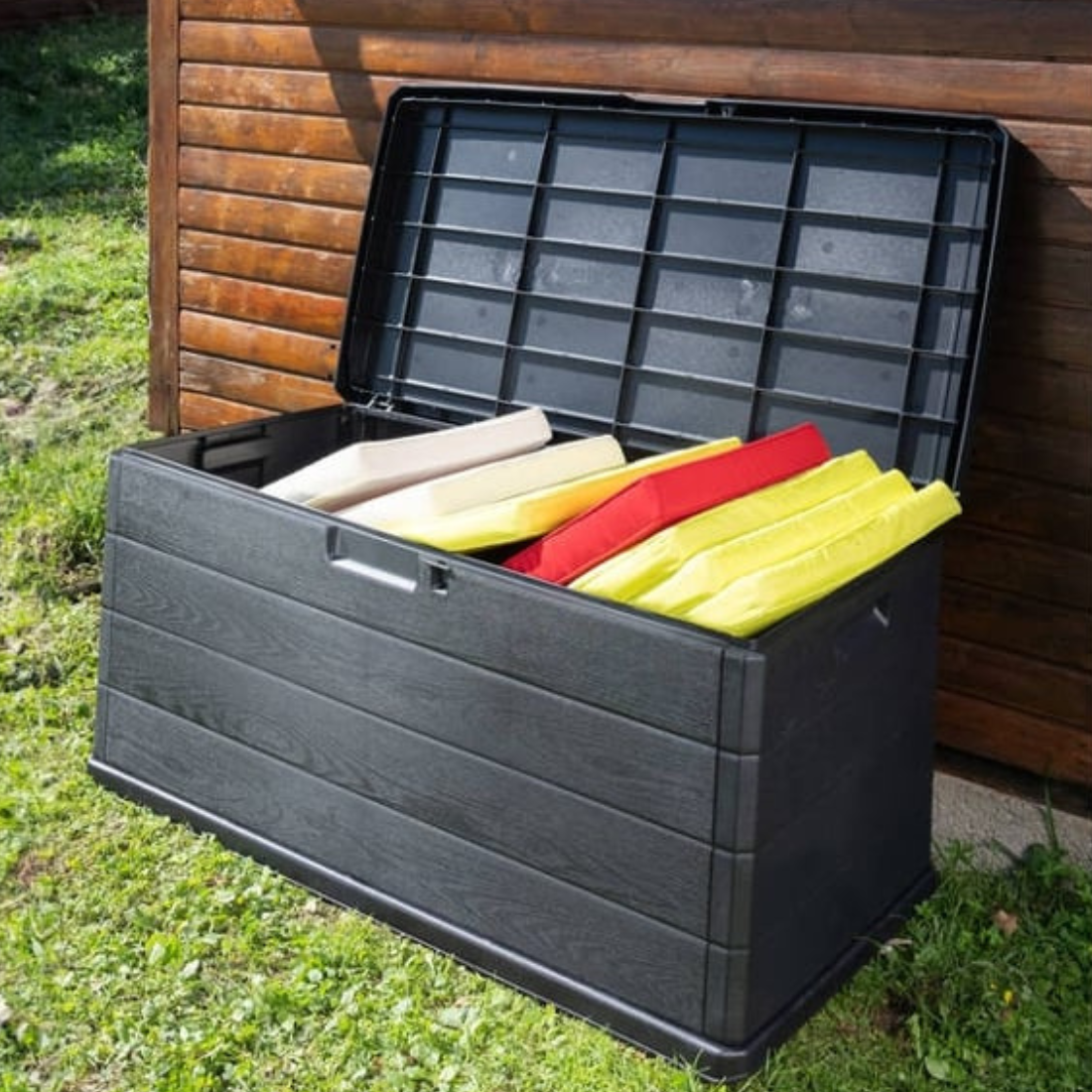 Baú de arrumação IPAE PROGARDEN, de plástico com efeito madeira, de cor cinzenta, aberto e exibido em ambiente exterior.