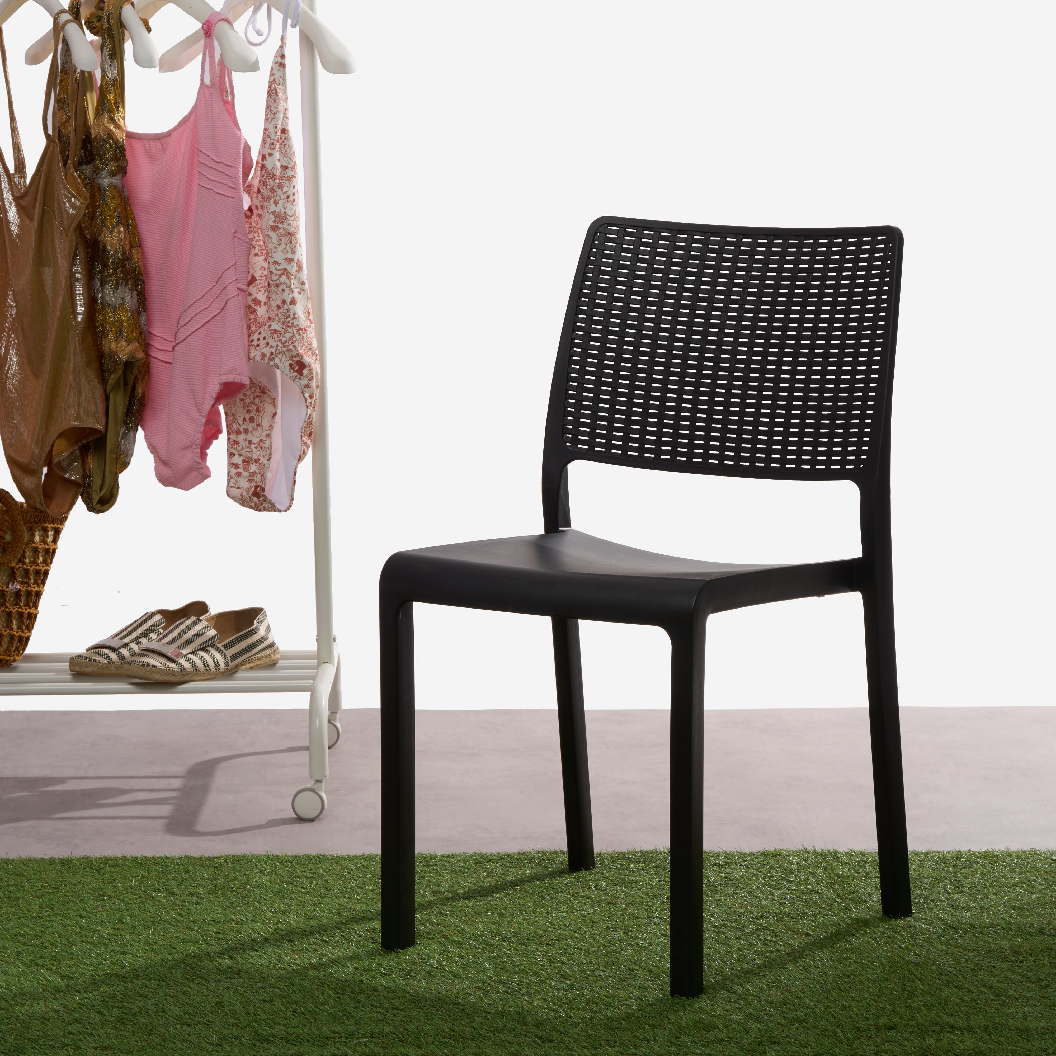 Cadeira IPAE PROGARDEN em plástico, de cor cinzenta, com encosto em acabamento trançado. Exibida em ambiente exterior.