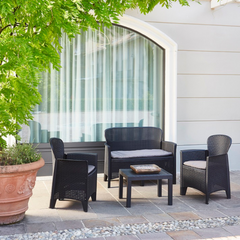 Conjunto de 2 cadeirões, 1 cadeirão duplo e uma mesa IPAE PROGARDEN, de cor preta, com acabamento entrançado e assento com almofada. Exibido m ambiente exterior.