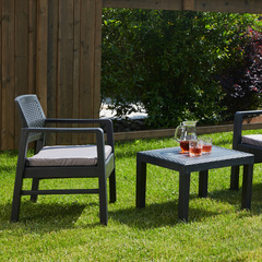 Conjunto de duas cadeiras baixas e uma mesa baixa quadrada IPAE PROGARDEN, da cor cinzenta, com almofada no assento e padrão entrançado. Exibido em ambiente exterior. 