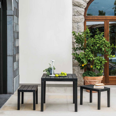 Conjunto de mesa e dois bancos IPAE PROGARDEN em plástico, de cor preta e com ranhuras . Exibido em ambiente exterior. 
