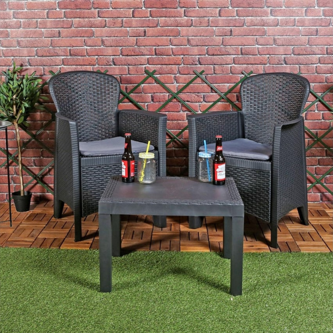 Conjunto de 2 cadeirões e uma mesa com 4 pés de apoio IPAE PROGARDEN, de cor cinzenta, com acabamento entrançado e assento com almofada. Exibido em ambiente exterior. 