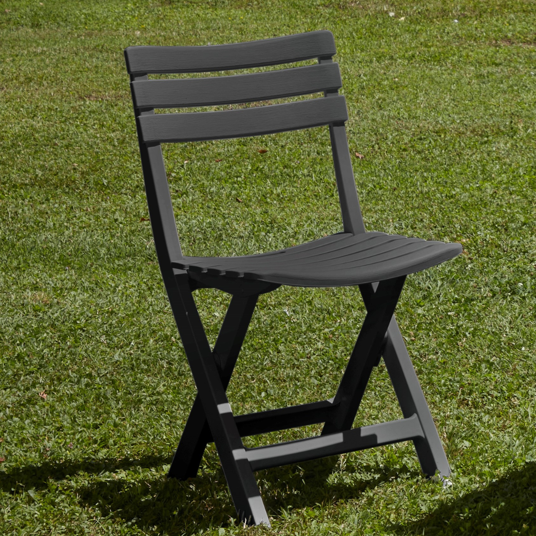 Cadeira dobrável IPAE PROGARDEN, em plástico com efeito madeira, da cor cinza. Exibida em ambiente exterior. 