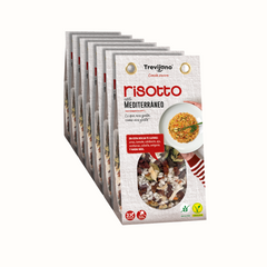 Risotto Mediterraneo em embalagem de cartão e plástico transparente, com uma mistura de vegetais desidratados, ervas aromáticas e especiarias. A embalagem tem um rótulo com o nome do produto e informações nutricionais. Fundo branco.